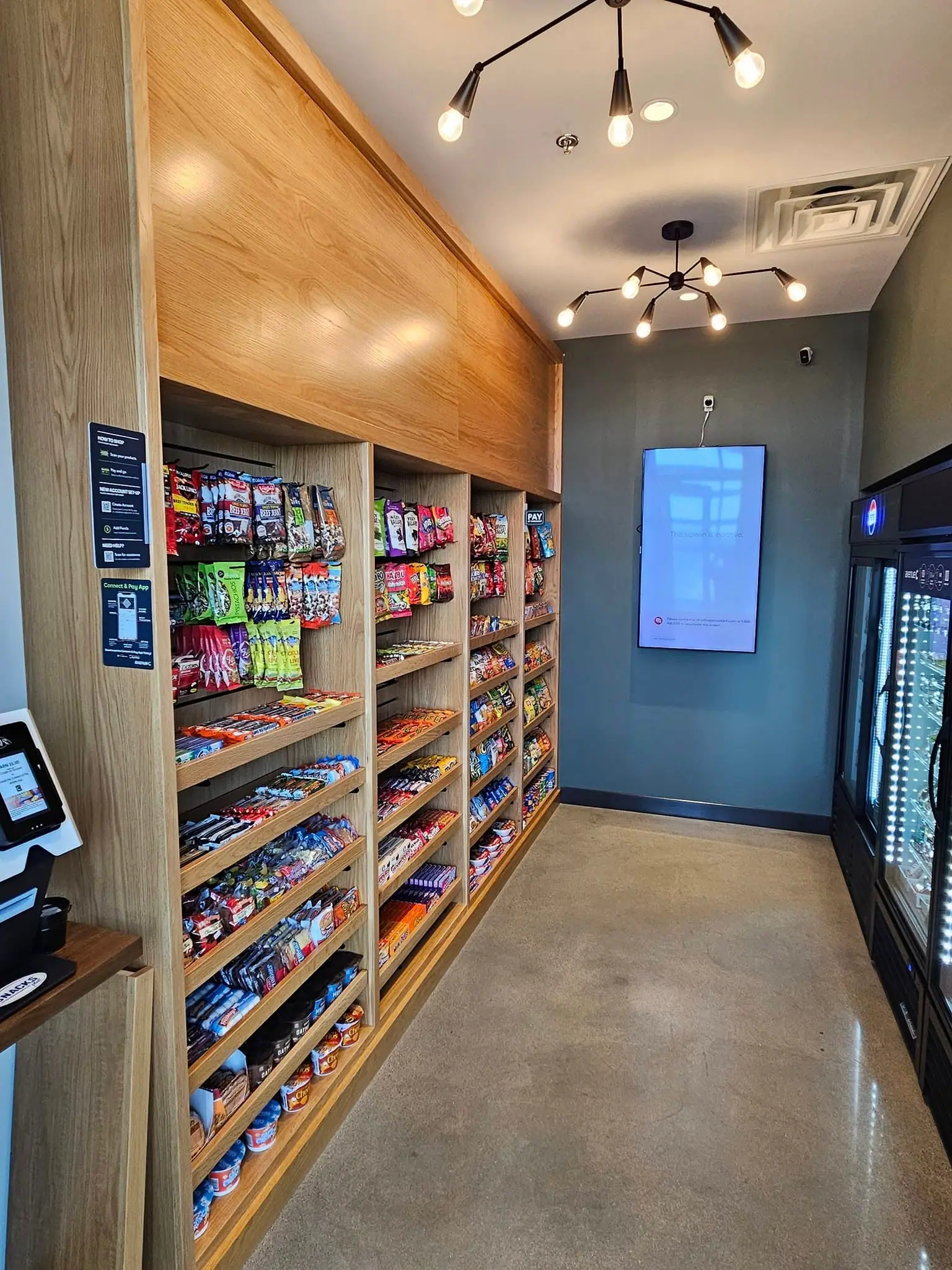 Micro market with wood shelving, glass-door coolers and a self-checkout kiosk